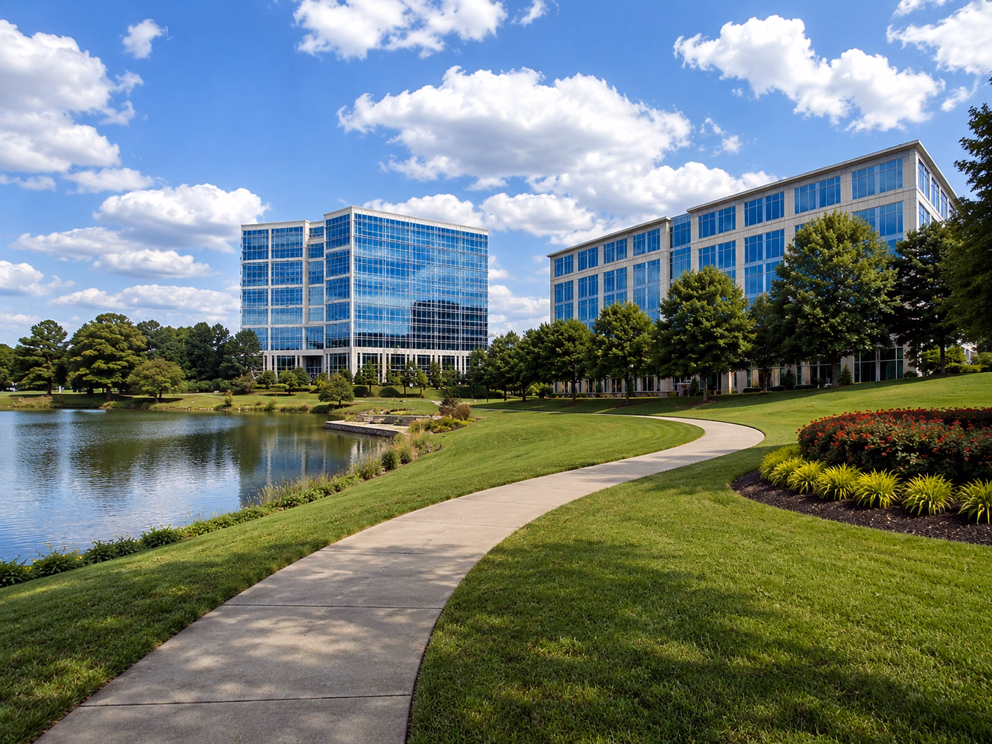 Concept photography of an office campus with a lake, winding walkway, and manicured lawns under mature trees