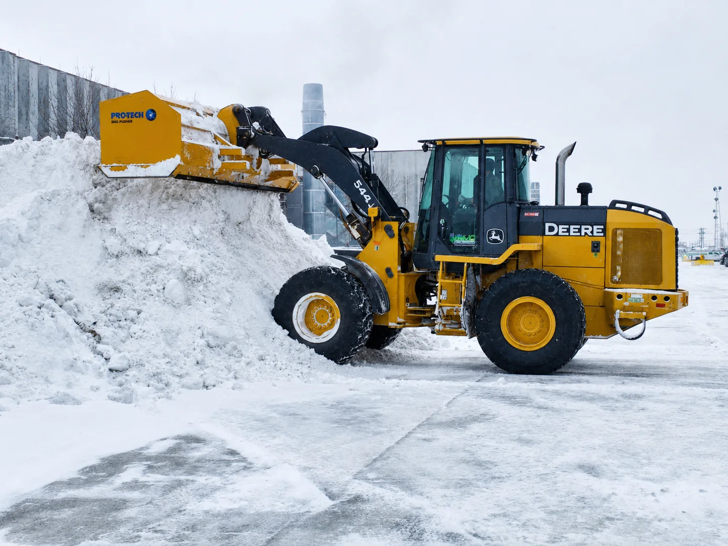 A wheel loader with a snow pusher stacking snow in a cleared commercial lot