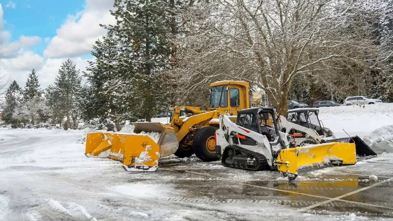 Snow removal fleet with plows clearing a commercial lot